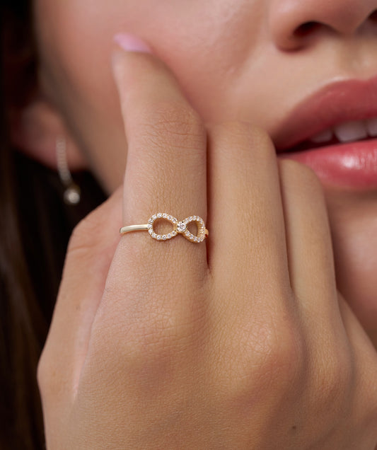 Gold infinity ring on a finger with a blurred background