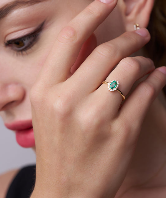 Close-up of a hand wearing a gold ring with a green gemstone, blurred background
